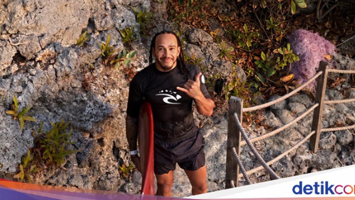 Lewis Hamilton membawa papan selancar merah di jalur berbatu kawasan Uluwatu, Bali.